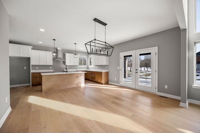 kitchen with white cabinets, sink, an island with sink, and wall chimney exhaust hood