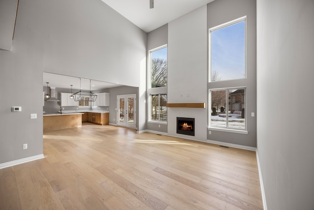 unfurnished living room featuring ceiling fan, a towering ceiling, a large fireplace, and light wood-type flooring