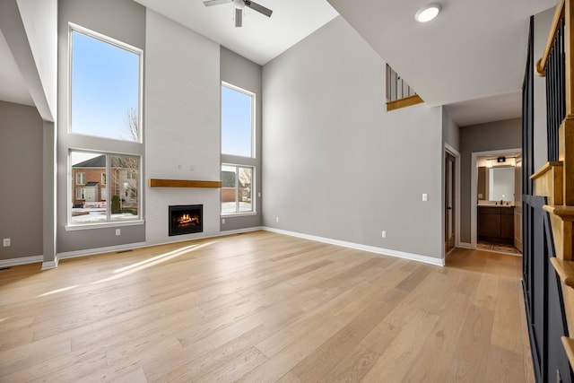 unfurnished living room with a high ceiling, ceiling fan, a large fireplace, and light hardwood / wood-style floors