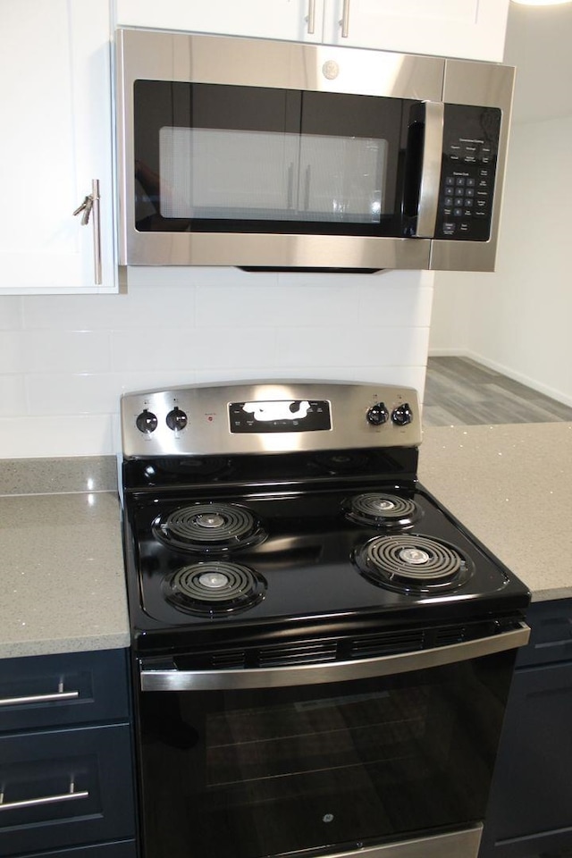 kitchen with hardwood / wood-style floors, light stone countertops, backsplash, and appliances with stainless steel finishes