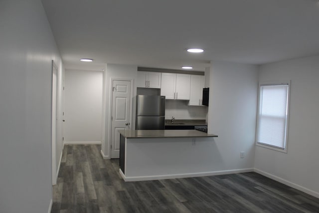 kitchen with white cabinetry, dark wood-type flooring, tasteful backsplash, kitchen peninsula, and stainless steel fridge