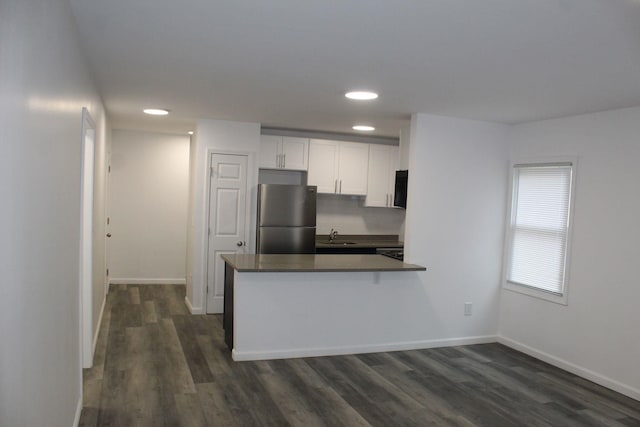 kitchen with kitchen peninsula, stainless steel fridge, dark wood-type flooring, sink, and white cabinetry