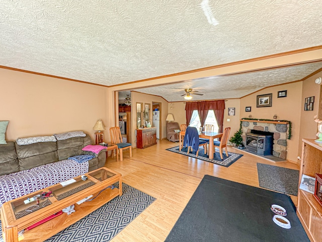 living room with ornamental molding, a textured ceiling, ceiling fan, hardwood / wood-style floors, and a wood stove