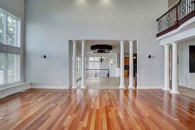 unfurnished living room featuring a towering ceiling, light wood-type flooring, and an inviting chandelier