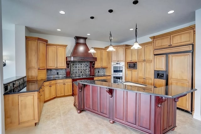 kitchen with built in appliances, custom range hood, an island with sink, and a breakfast bar area