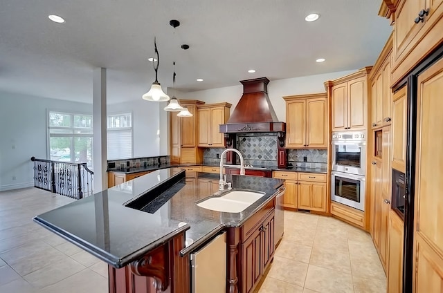 kitchen with sink, wall chimney exhaust hood, hanging light fixtures, a center island with sink, and light tile patterned flooring