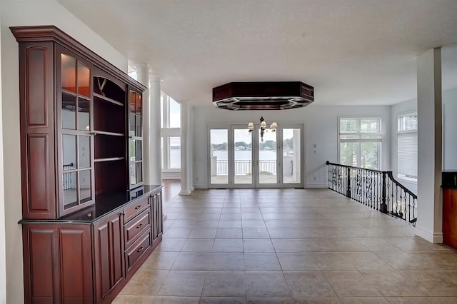 unfurnished living room featuring decorative columns, light tile patterned floors, a textured ceiling, and a notable chandelier