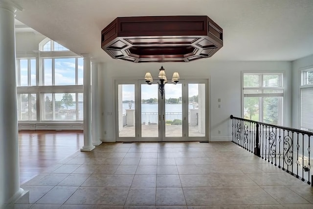 entryway with ornate columns, a water view, a healthy amount of sunlight, and an inviting chandelier