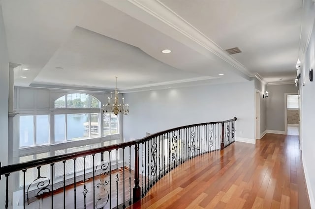 corridor with a chandelier, hardwood / wood-style floors, a tray ceiling, and ornamental molding