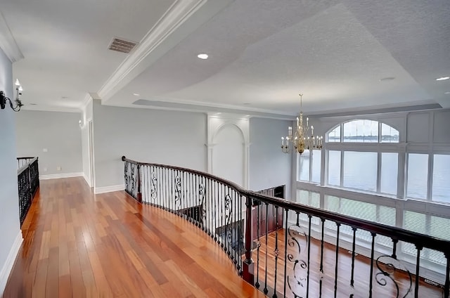 corridor featuring an inviting chandelier, ornamental molding, a textured ceiling, a tray ceiling, and wood-type flooring