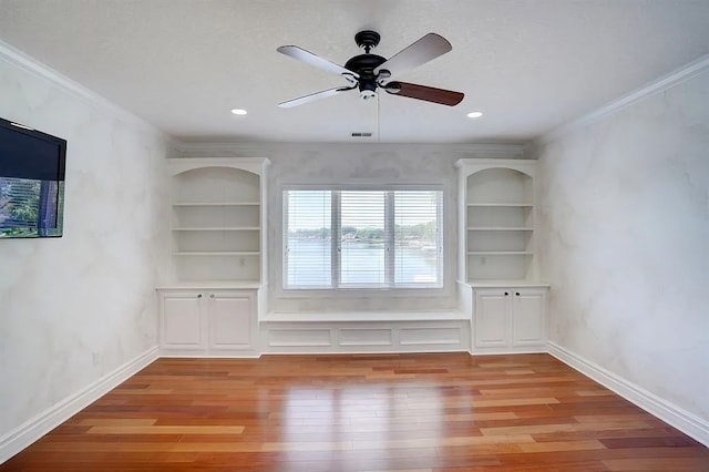 empty room featuring built in shelves, ceiling fan, crown molding, and light hardwood / wood-style flooring