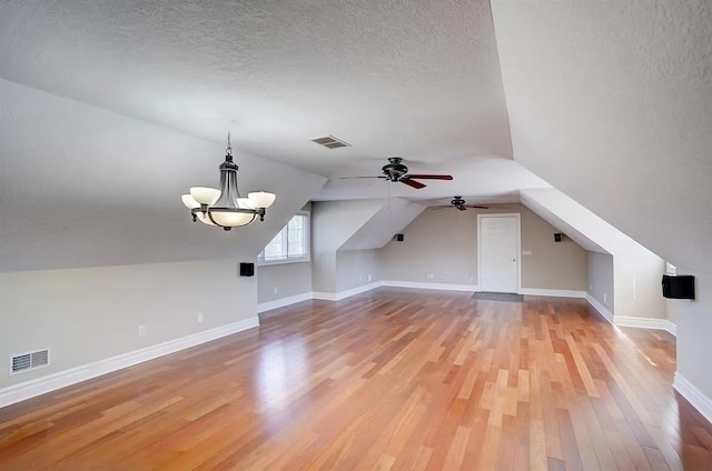 bonus room with lofted ceiling, ceiling fan with notable chandelier, wood-type flooring, and a textured ceiling