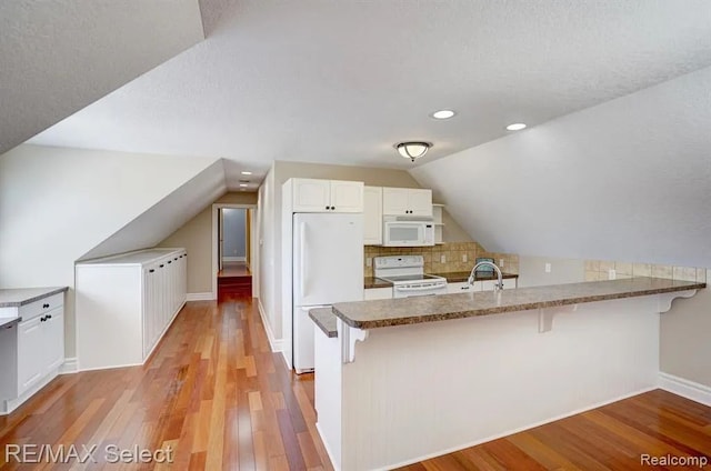 kitchen featuring light wood-type flooring, white appliances, kitchen peninsula, and vaulted ceiling