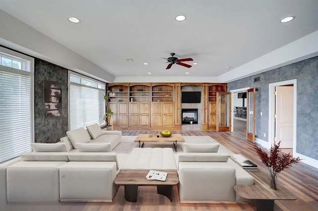 living room with ceiling fan, a large fireplace, and light wood-type flooring