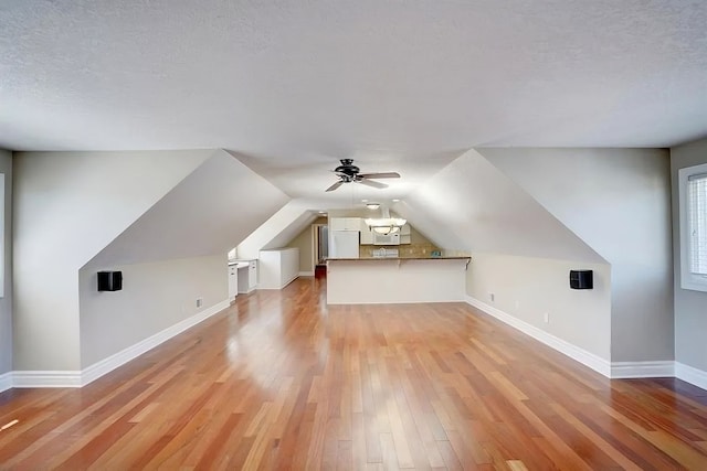 additional living space with a textured ceiling, light hardwood / wood-style flooring, ceiling fan, and lofted ceiling