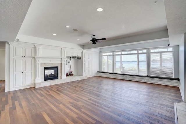 unfurnished living room with ceiling fan, a baseboard heating unit, wood-type flooring, a textured ceiling, and a tiled fireplace