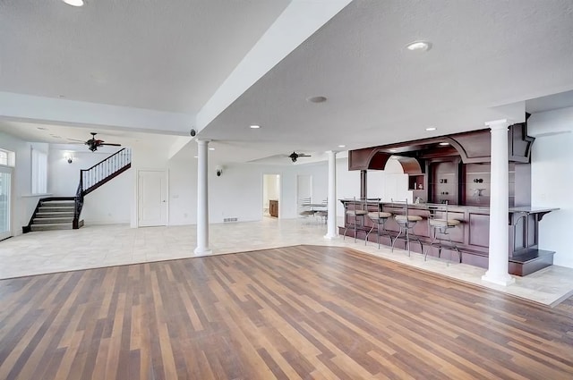 unfurnished living room with a textured ceiling, ceiling fan, light hardwood / wood-style floors, and indoor bar