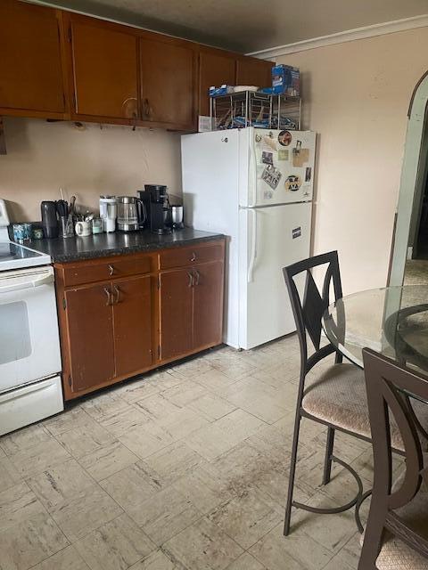621 E Michigan Ave, Grass Lake, MI 49240 - kitchen with white appliances, crown molding, dark countertops, and brown cabinets