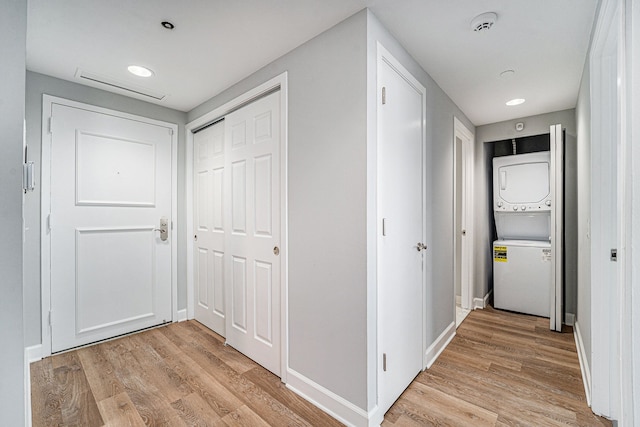 hall with stacked washer / drying machine and light hardwood / wood-style flooring