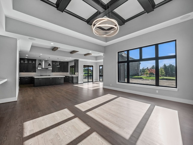 unfurnished living room with dark wood-type flooring, a healthy amount of sunlight, coffered ceiling, and a notable chandelier