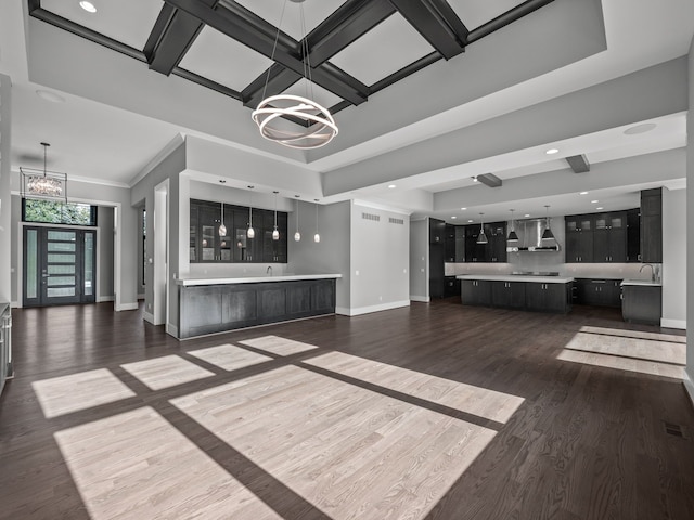 unfurnished living room featuring sink, coffered ceiling, dark hardwood / wood-style flooring, a chandelier, and ornamental molding