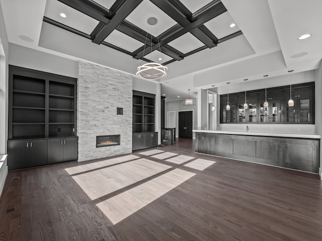 unfurnished living room featuring an inviting chandelier, coffered ceiling, a stone fireplace, dark hardwood / wood-style floors, and built in features