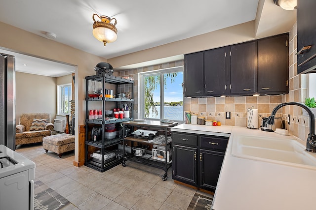 kitchen with sink, backsplash, stainless steel fridge, light tile patterned flooring, and range