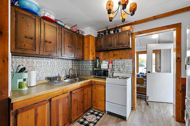 kitchen with sink, tasteful backsplash, light hardwood / wood-style flooring, white range with gas stovetop, and a chandelier