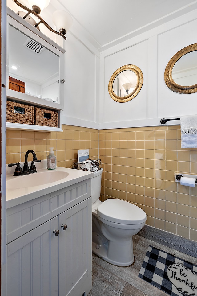 bathroom with wood-type flooring, vanity, toilet, and tile walls