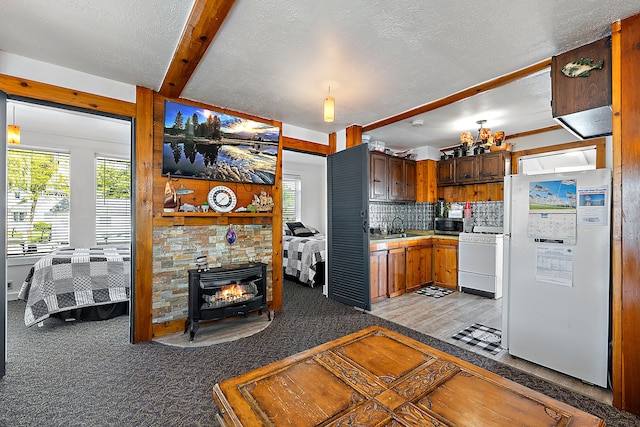 kitchen with tasteful backsplash, white appliances, sink, beamed ceiling, and a wood stove