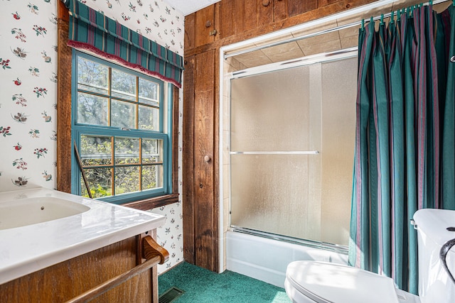 full bathroom featuring wood walls, toilet, vanity, and combined bath / shower with glass door