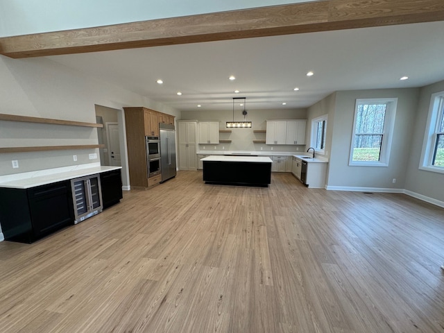 kitchen with a center island, beverage cooler, pendant lighting, white cabinets, and light wood-type flooring