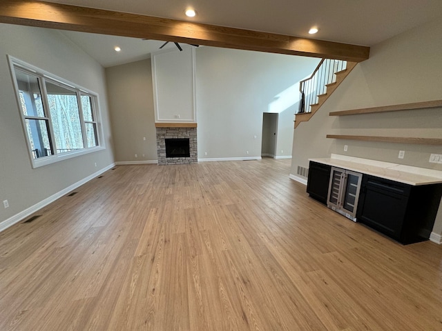 unfurnished living room featuring ceiling fan, wine cooler, beamed ceiling, a fireplace, and light wood-type flooring