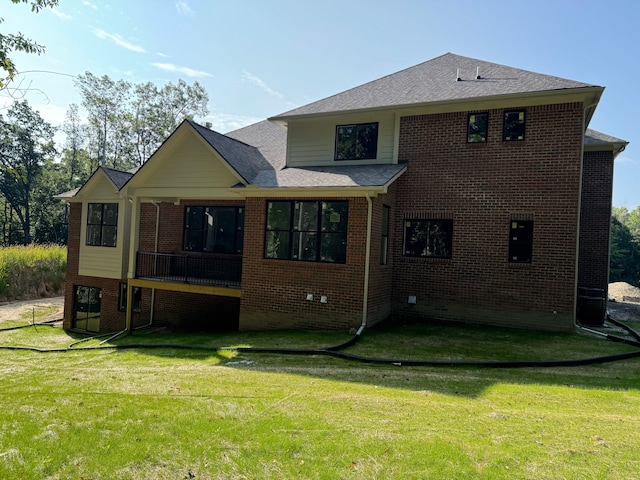 back of property featuring roof with shingles, brick siding, and a lawn