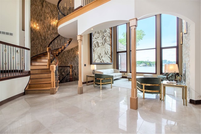 foyer featuring a healthy amount of sunlight, a water view, a high ceiling, and decorative columns