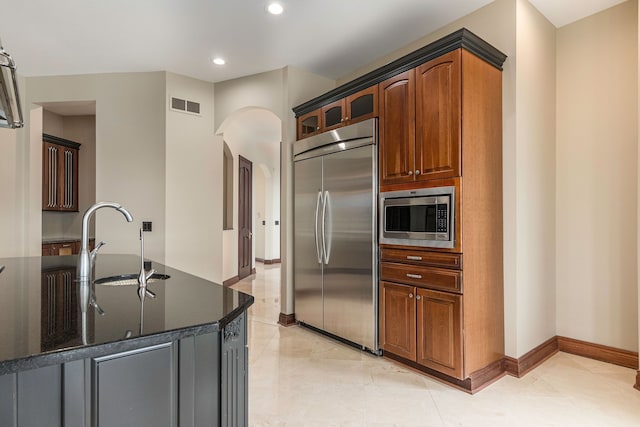 kitchen with built in appliances, dark stone countertops, and sink