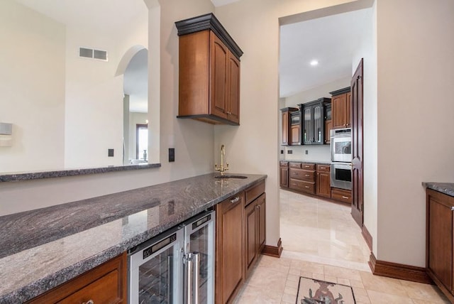 kitchen with sink, stainless steel double oven, beverage cooler, dark stone counters, and light tile patterned floors