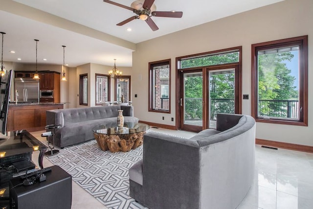 tiled living room with ceiling fan with notable chandelier