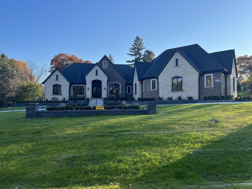 french provincial home featuring stone siding, brick siding, and a front lawn