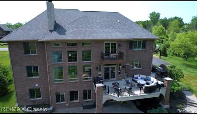 rear view of property with outdoor lounge area, brick siding, a chimney, and a balcony