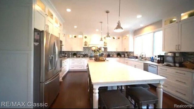 kitchen with glass insert cabinets, appliances with stainless steel finishes, decorative light fixtures, a center island, and backsplash