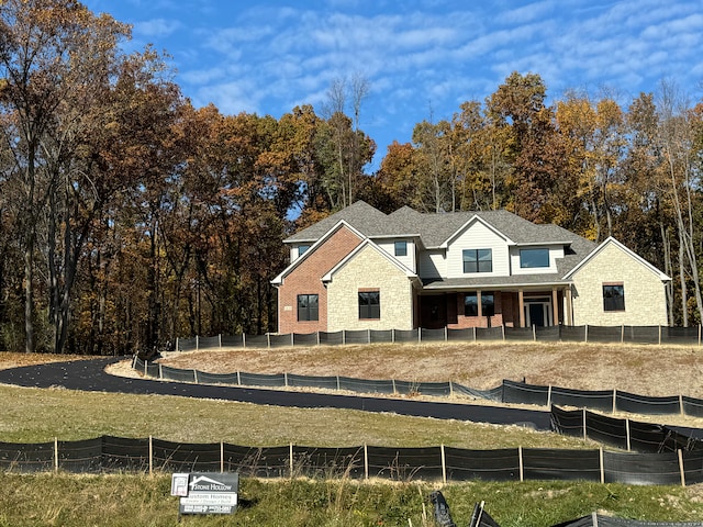 view of front of property with stone siding, a shingled roof, and fence