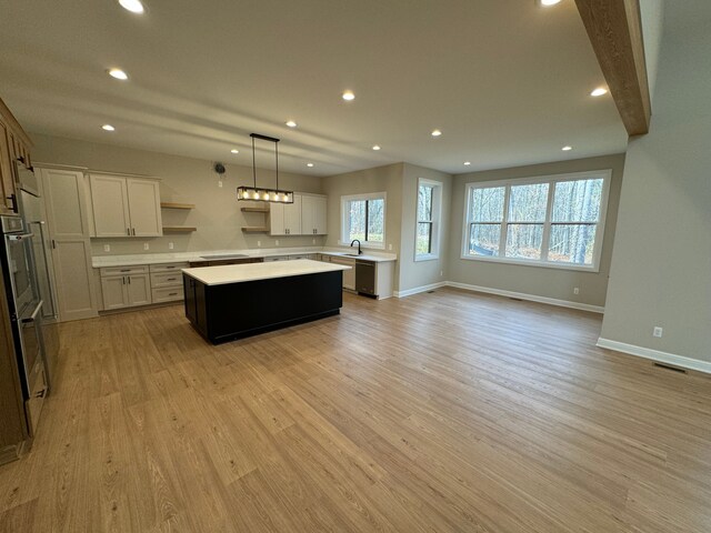 kitchen with sink, white cabinetry, a center island, decorative light fixtures, and light wood-type flooring