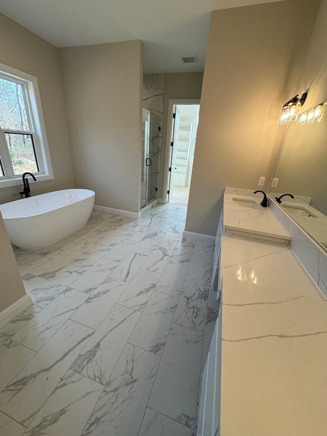 bathroom featuring marble finish floor, a marble finish shower, double vanity, a freestanding bath, and baseboards