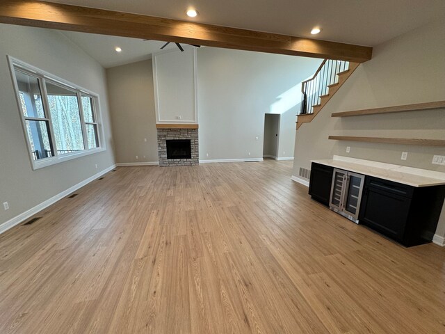 unfurnished living room with wine cooler, lofted ceiling with beams, a stone fireplace, light wood-type flooring, and baseboards