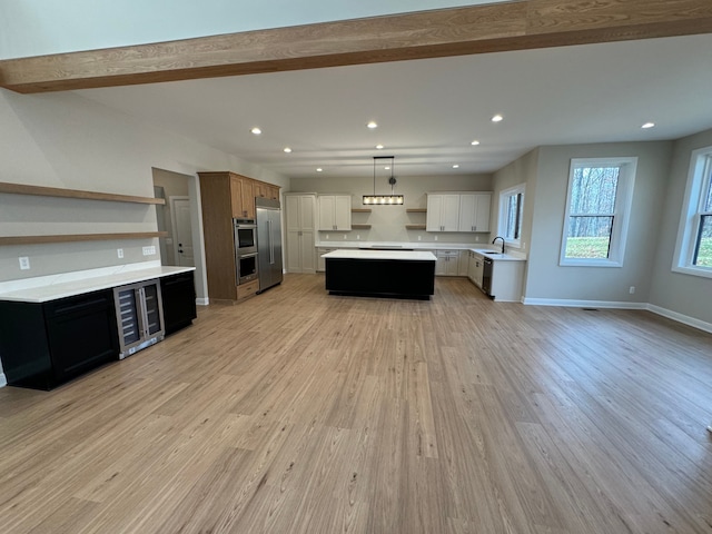 kitchen featuring a center island, light wood finished floors, stainless steel appliances, a sink, and beverage cooler