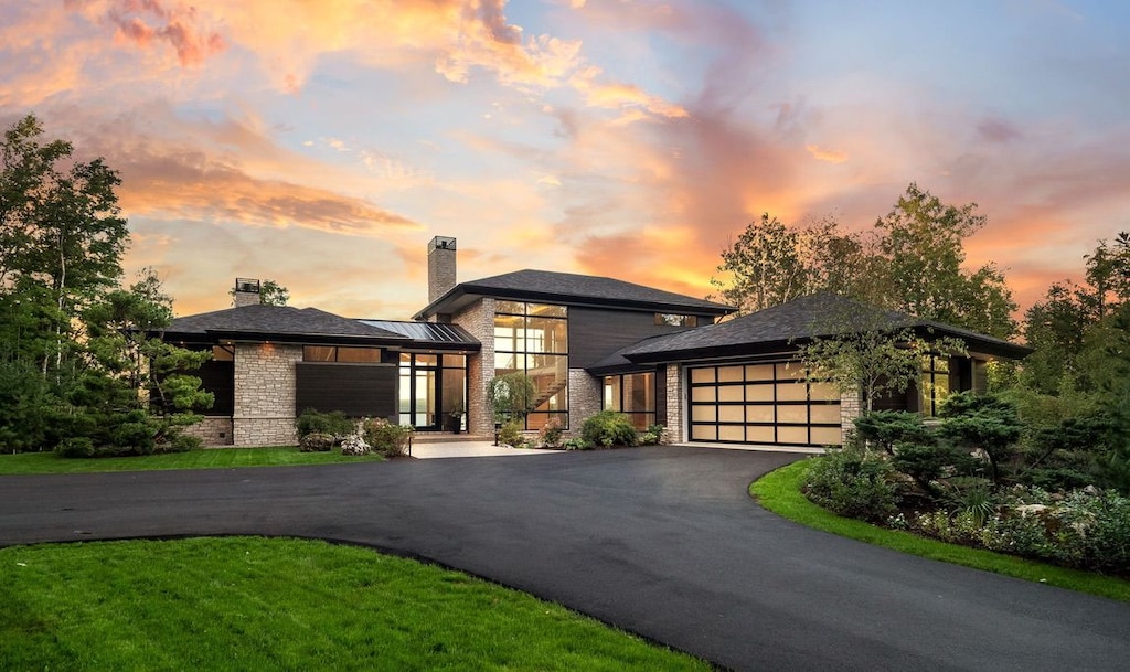prairie-style house with stone siding, a chimney, a garage, and aphalt driveway