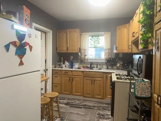 kitchen featuring light brown cabinetry, white refrigerator, gas stove, and sink