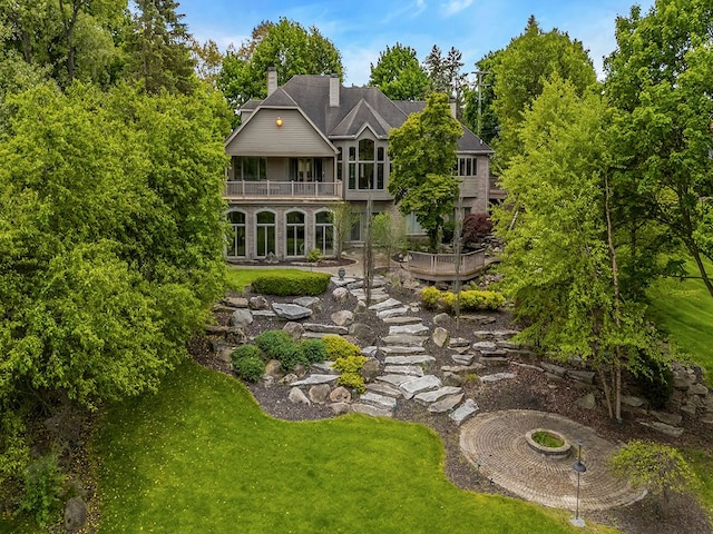 back of house featuring a lawn, a balcony, and an outdoor fire pit