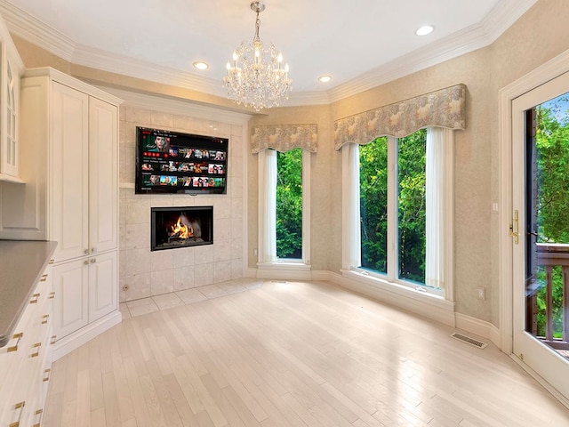 interior space featuring a chandelier, light hardwood / wood-style floors, crown molding, and a tiled fireplace